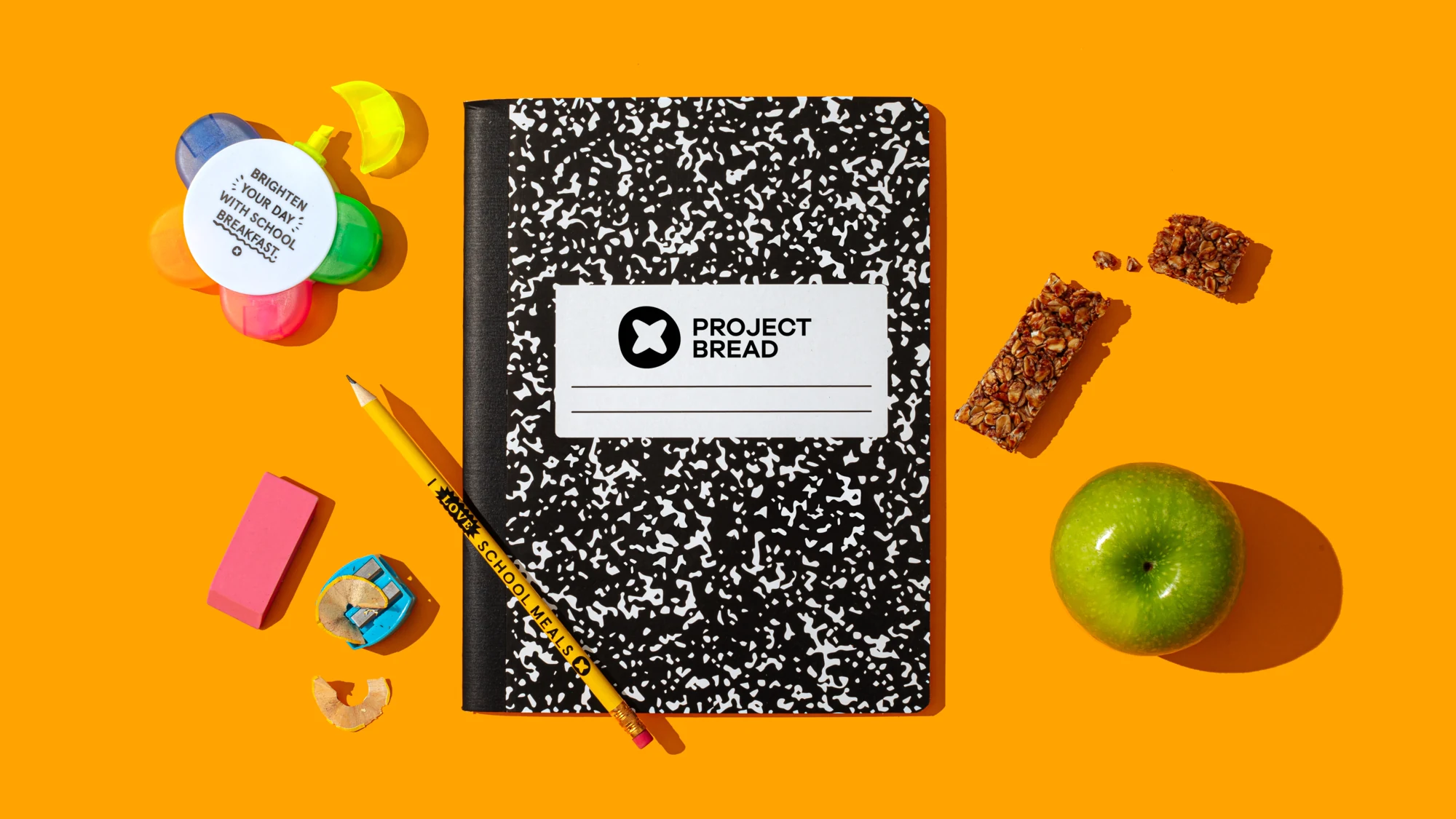 Project Bread branded notebook surrounded by school supplies and snacks on an orange background